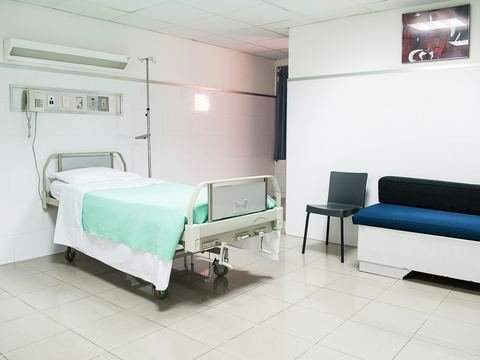 A calm, bright hospital room with a bed and a sofa